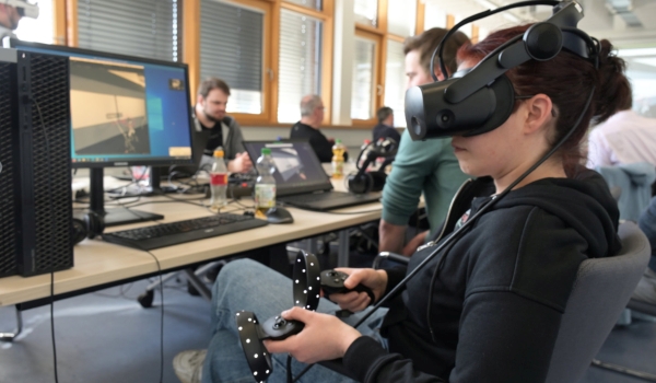 Frau mit VR-Brille und Controllern am Computer sitzend