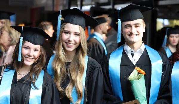 Zwei Absolventinnen und ein Absolvent, glücklich in Talar und Hut auf Absolventenfeier