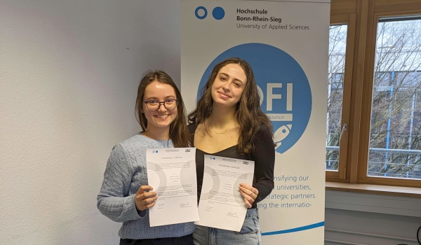 Zwei lächelnde Studentinnen präsentieren ihre Urkunde