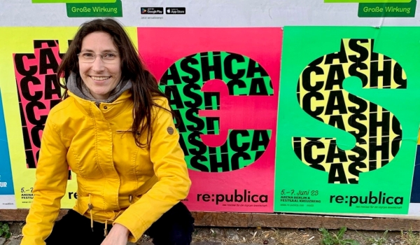 Junge Frau in der Hocke, vor bunten re:publica-Plakaten auf der Straße