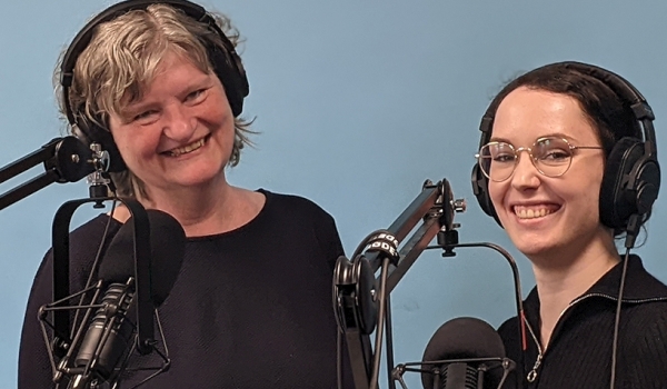Zwei lächelnde Frauen mit Kopfhörern bei der Aufnahme eines Podcasts