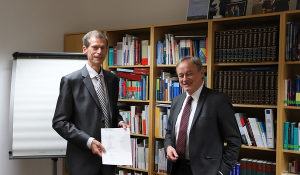 Präsident Hartmut Ihne und Professor Manfred Kaul mit Urkunde im Büro vor Bücherregal