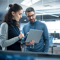 Eine Frau und ein Mann stehen mit Laptop im Serverraum.