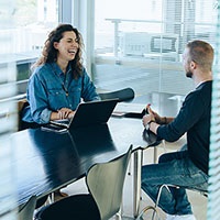 Eine Frau und ein Mann sitzen sich beim Recruiting mit Laptop gegen&uuml;ber.